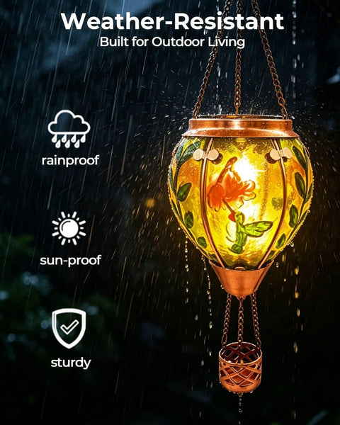 Glass Hot Air Balloon Solar Lantern With Flame Hand Painted Artwork Realistic Flickering Flame Hummingbird Accent Rustproof Metal Outdoor Solar Light For Garden Or Yard Easy Setup And Eco Friendly illuminated in the rain, showcasing weather resistance.
