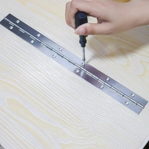 Installing Tough as Nails Heavy Duty 12 Inch Stainless Steel Piano Hinges 4 Pack With 48 Screws on wooden surface with screwdriver