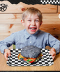 Boy holding a black and white checkered tray with a large black burger, showcasing Set Of Three 13 X 10 Inch Rectangular Checkered Serving Trays Black And White Racer Platters For Snacks Desserts And Tailgate Game Day Block Party Vibes.