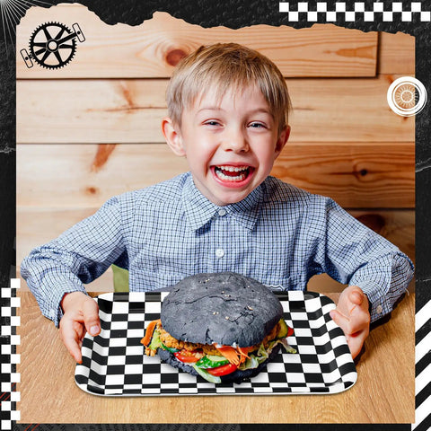 Boy holding a black and white checkered tray with a large black burger, showcasing Set Of Three 13 X 10 Inch Rectangular Checkered Serving Trays Black And White Racer Platters For Snacks Desserts And Tailgate Game Day Block Party Vibes.