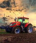 Red farm tractor, side-angle view on a freshly plowed field at sunset with large tires.