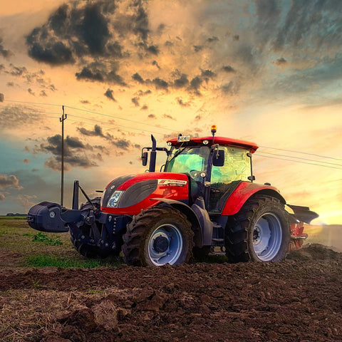 Red farm tractor, side-angle view on a freshly plowed field at sunset with large tires.
