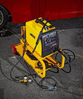 HEAVY DUTY YELLOW POWDER COATED STEEL WELDING CART WITH SMOOTH ROLLING CASTERS AND SLANTED WORK SURFACE BUILT TO CRUSH THE GRIND AND HAUL YOUR GEAR FAST positioned beside a red car.