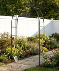 Iron Pergola Garden Arbor For Weddings And Backyards, 7.9 feet high black metal arch in garden setting among flowers
