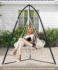 Two Person Hanging Hammock Chair With Thick Cushions And Boho Macrame Swing For Indoor Outdoor Use On Porch Balcony Or Bedroom Cozy And Comfy Relax In Comfort With Soft Removable Cushion And Tassels outside a home.