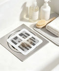 Hair Drain Stickers Disposable Hair Catcher for Shower Drain on a silver drain with caught hair strands nearby.