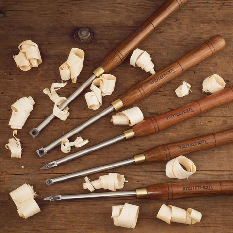 Badass Five Piece Wood Turning Lathe Chisel Set Featuring Rock Solid Tungsten Carbide Tips And Built Tough Square Stainless Handles on a wooden surface with shavings.