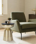 Hourglass Accent Side Table With Natural Granite Top And Brushed Brass Base beside green armchair in modern living room.