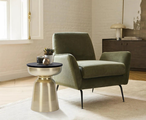 Hourglass Accent Side Table With Natural Granite Top And Brushed Brass Base beside green armchair in modern living room.
