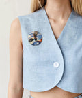 Close-up of a woman wearing a Dope Sunset Airplane Button Pin on a blue vest, part of the Set Of Five 2.4 Inch Round Metal Badges.