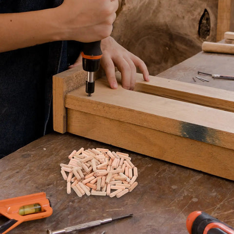 Person using a drill for furniture assembly with a pile of Wooden Dowel Pins M8x30mm For Furniture Assembly in beige on the table.