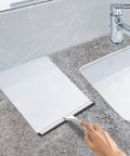 Side view of 10-inch stainless steel bathroom shower squeegee on a stone countertop beside a chrome faucet.