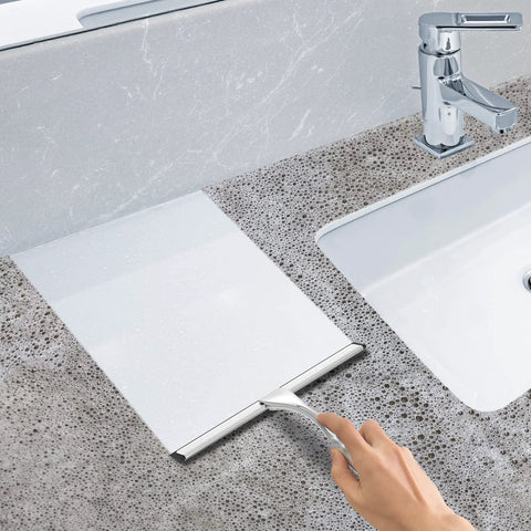 Side view of 10-inch stainless steel bathroom shower squeegee on a stone countertop beside a chrome faucet.