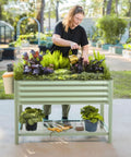 Raised Garden Bed V Series 2 Ft By 4 Ft With Legs And Storage Rack for patio shown with plants and woman gardening, olive green.