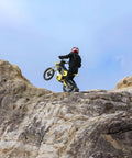 Rider on a Heavy Duty Electric Dirt Bike Two Pack climbing rocky terrain with a red helmet for off road adventures.