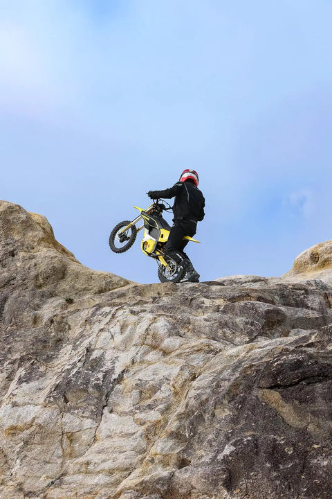 Rider on a Heavy Duty Electric Dirt Bike Two Pack climbing rocky terrain with a red helmet for off road adventures.