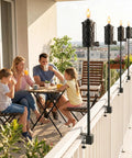 Family enjoying balcony with 6 Pack Garden Torch With Universal Clamp, 16 Oz Citronella Oil Outdoor Torches on railing, evening lighting.