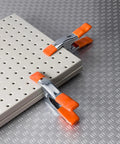 Heavy Duty Spring Clamp Set 4-Inch And 6-Inch Clamps With 1-Inch And 2-Inch Jaw Openings holding a perforated board on metal surface