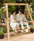 Couple sitting on a wooden garden swing surrounded by plants and flowers on a patio.