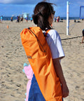 Person carrying Low Profile Beach Chair Set Of 2 For Adults And Kids in orange bag on sandy beach, sunny day.
