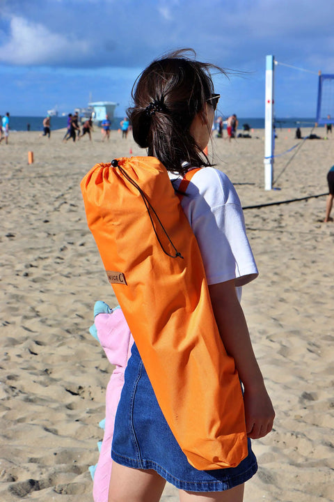 Person carrying Low Profile Beach Chair Set Of 2 For Adults And Kids in orange bag on sandy beach, sunny day.