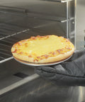 Gloved hand placing pizza on Aluminum 6 Inch Pizza Screen Pack Of 144 For Crispy Crust And Fast Even Baking Lightweight And Stackable in oven