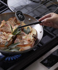 Digital Instant Read Kitchen Thermometer With Pivoting Backlit Display For Easy Reading From Any Angle Ultra Fast Under Six Seconds Wide Minus Forty To Four Hundred Eighty Two Fahrenheit Range For Grill Masters Baking Candy Making And More Black in use checking temperature of meat in frying pan on stove.