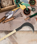 Long Handle Hand Scythe for Weeding and Lawn Care, Manganese Steel Manual Weeding Tool on wooden table with garden tools