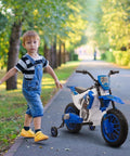Child walking beside blue 12V kids motorcycle with treaded tires and training wheels on a park path, lush greenery in background.