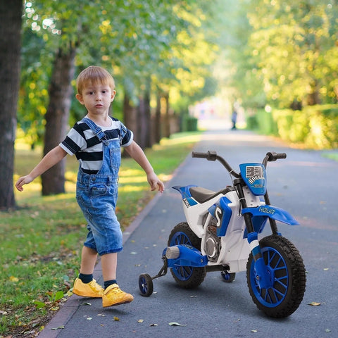 Child walking beside blue 12V kids motorcycle with treaded tires and training wheels on a park path, lush greenery in background.