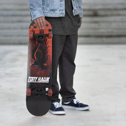 Person holding Tony Hawk skateboard with eagle graphic, an alternative to 31 Inch Pro Trucks Skateboard With Full Grip Tape And 9 Ply Maple Deck For Easy Cruising And All Skill Levels Signature Series Longboard Style Cruiser Built For Beginners To Pros