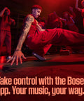 Group of dancers performing energetically in a dimly lit room with text overlay promoting the Bose app for music control.