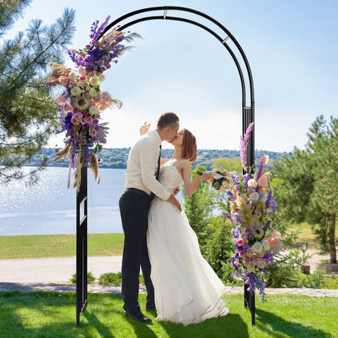 Bride and groom kissing under 7.2 Ft Outdoor Steel Garden Arch Arbor With Stakes, Wide Sturdy Black Metal Archway with floral decor.