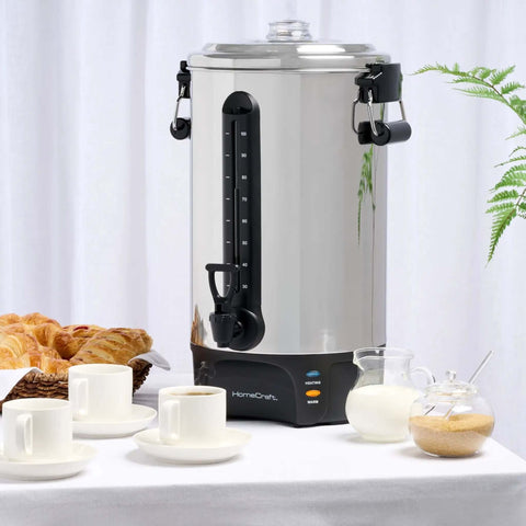 100 Cup Coffee Urn And Hot Beverage Dispenser With Dripless Faucet, stainless steel on a table with pastries and cups, side view