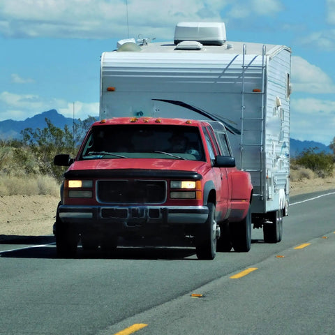 Red truck towing a white camper trailer on a desert road, demonstrating the Slick Trailer Wiring Junction Box For Rv And Camper Lights Seven Gang Automotive Connector Rewiring Kit With Bold Markings For Quick Plugging And Hassle Free Hookup Installation.