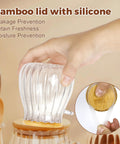 Hand holding refillable sugar jar with bamboo lid and spoon, silicone seal, 15 oz glass canister for coffee bar decor.