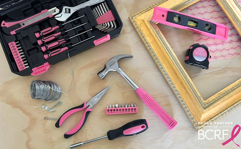 39 Piece General Household Tool Set In Toolbox Storage Case With Essential Hand Tools For Everyday Home Repairs DIY And Crafts Pink Ribbon Edition Includes Hammer Pliers Wrench Tape Measure Utility Knife Magnetic Level And More displayed on wood surface with pink and black accents.