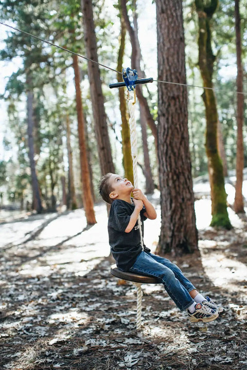 Child using Zip Line Kit 150 Feet With Seat And Carabiner Heavy Duty One Quarter Inch Galvanized Cable Backyard Fun For Families Supports Up To 350 Lbs Weather Resistant Easy Setup For Hours Of Outdoor Adventure in forest