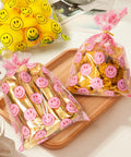 Clear Treat Bags With Twist Ties 5x9 Inches 100 Pack Happy Face Print Party Fav Bags with snacks and candies displayed on a tray.