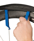Person using blue tire levers from On The Go Cyclist Essential Tool Kit With Tire Levers, Fold Up Hex And Screwdriver, Emergency Tire Boots, Pre Glued Tube Patches, And A Handy Wallet Built For Quick Fixes At Home Or On The Road on a bicycle wheel.