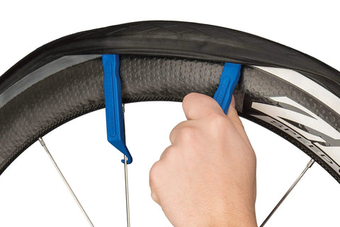Person using blue tire levers from On The Go Cyclist Essential Tool Kit With Tire Levers, Fold Up Hex And Screwdriver, Emergency Tire Boots, Pre Glued Tube Patches, And A Handy Wallet Built For Quick Fixes At Home Or On The Road on a bicycle wheel.