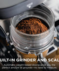 Brew Like A Pro At Home With This Triple Threat Espresso And Drip Coffee Maker Featuring Rapid Cold Brew Options Alongside Reliable Dual Shot Settings In Sleek Gunmetal Finish showing built-in grinder with coffee grounds.