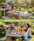 Family using Buffalo Plaid Picnic Table Cover Set With Bench Covers For 6 Foot Tables Waterproof Elastic Fitted Tablecloth Outdoor Ready Washable Black And White 30 By 72 Inch Tablecloth And Two 12 By 72 Inch Bench Covers outdoors in garden setting.