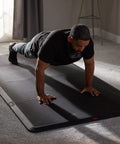 Man exercising on 4x8 Gym Flooring Mat For Peloton Bike Elliptical Treadmill And Home Gym Setup Non Slip Floor Pad For Hardwood Or Carpet Just Unroll And Transform Any Room Into A Home Gym Ideal For Spin HIIT Zumba Cardio Training