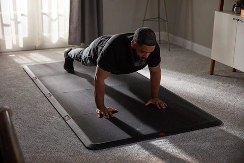 Man exercising on 4x8 Gym Flooring Mat For Peloton Bike Elliptical Treadmill And Home Gym Setup Non Slip Floor Pad For Hardwood Or Carpet Just Unroll And Transform Any Room Into A Home Gym Ideal For Spin HIIT Zumba Cardio Training