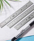 Three 6-inch stainless steel rulers on drafting paper, featuring metric and imperial markings from the Pro Grade Machinist Ruler Set