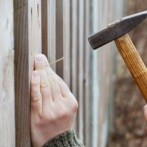 Person hammering Gold Finish Nail Kit With 600 Nails In Four Sizes For Picture Hanging And Woodworking into wooden fence
