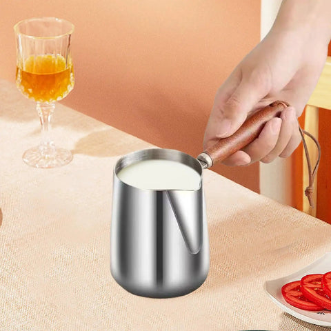 Hand holding Turkish Coffee Pot Stainless Steel Multipurpose Milk Frothing Pitcher And Coffee Kettle for Latte Art on table.