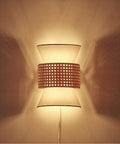 Two-Light Plug-In Or Hardwire Wall Sconce With Matte White Fabric Shade And Natural Rattan Accent glowing on wall