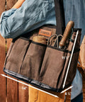Person carrying a Waxed Canvas Garden Tool Tote With Eight Exterior Pockets, Heavy Duty Tool Bag Storage Organizer, 14x11 inches.
